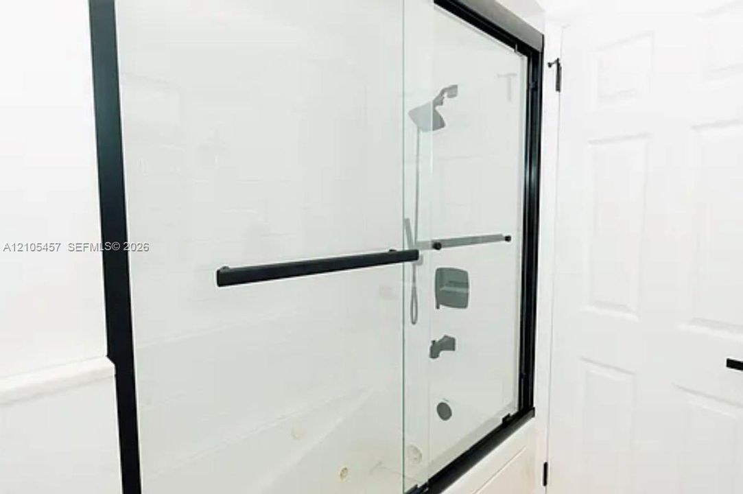Frameless glass shower enclosure with matte black hardware, integrated handheld showerhead, wall-mounted fixtures, and six-panel interior door