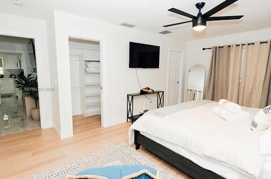 Room featuring wood-finish flooring, a matte black ceiling fan, and a walk-in closet with built-in shelving