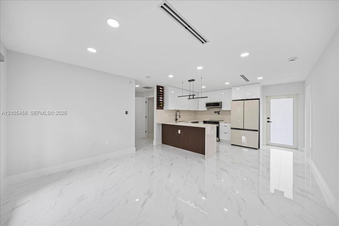 Open-concept living space featuring high-gloss tile flooring, recessed lighting, and a modern kitchen with white cabinetry