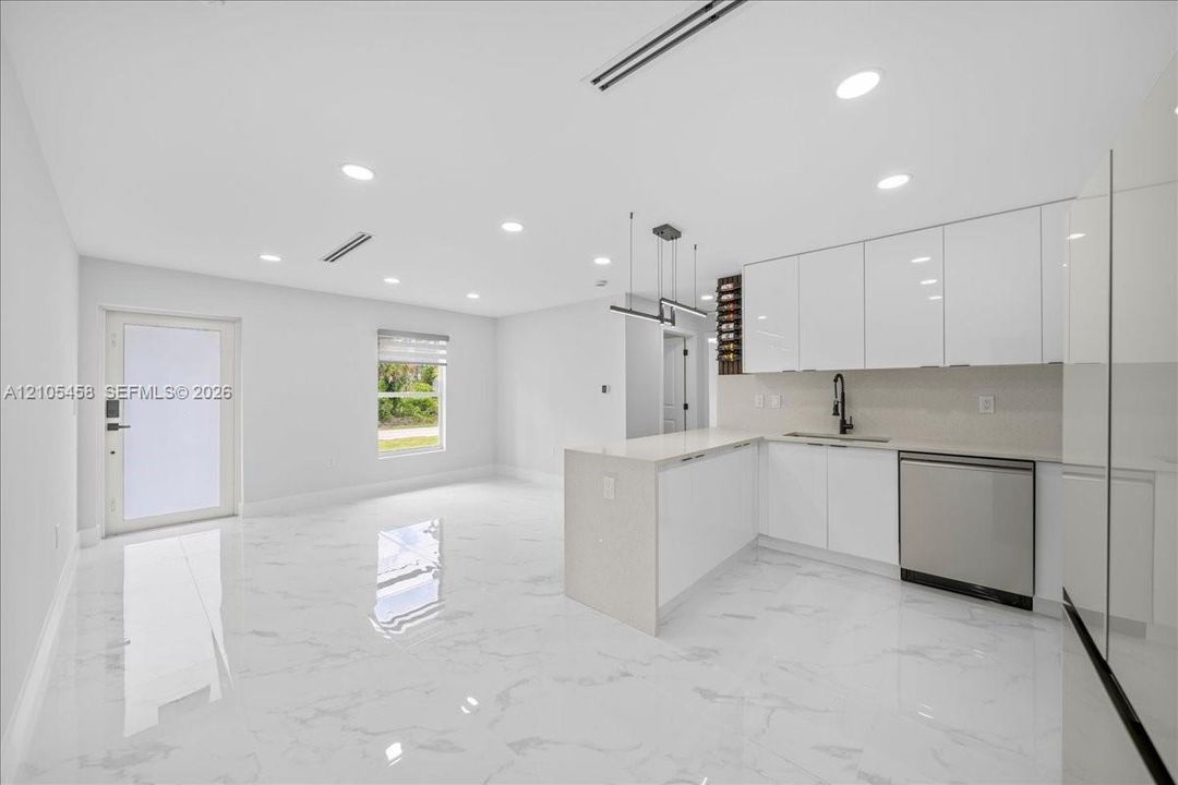 Open-concept layout featuring white high-gloss cabinetry, stainless steel dishwasher, integrated wine storage, white quartz countertops, and recessed lighting