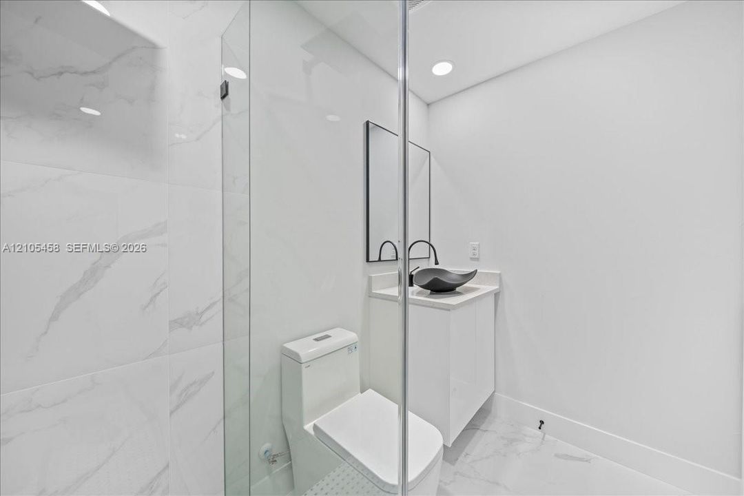Glass-enclosed shower with large format tile surround, recessed lighting, modern vanity with vessel sink, and wall-mounted mirror
