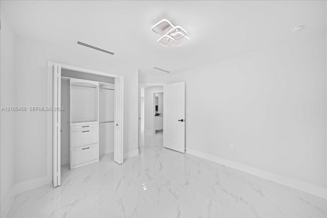 White tile flooring with subtle veining, modern ceiling light fixture, bi-fold closet doors, built-in closet organization with drawers, and a solid interior door