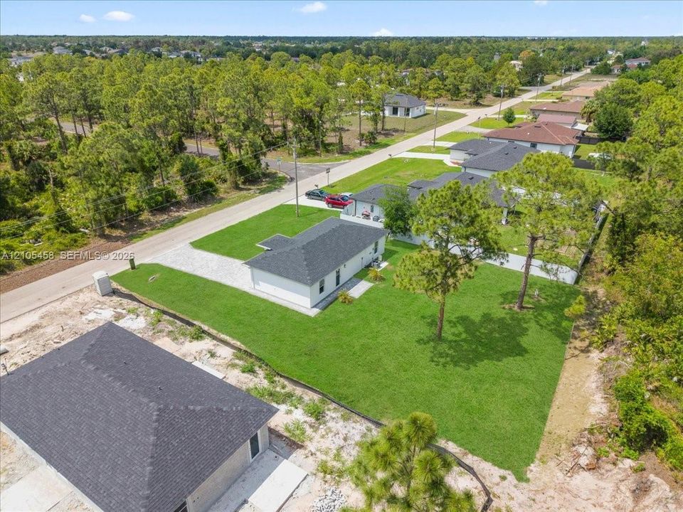 Manicured lawn, paved driveway, mature trees, newly installed roof, and surrounding natural foliage