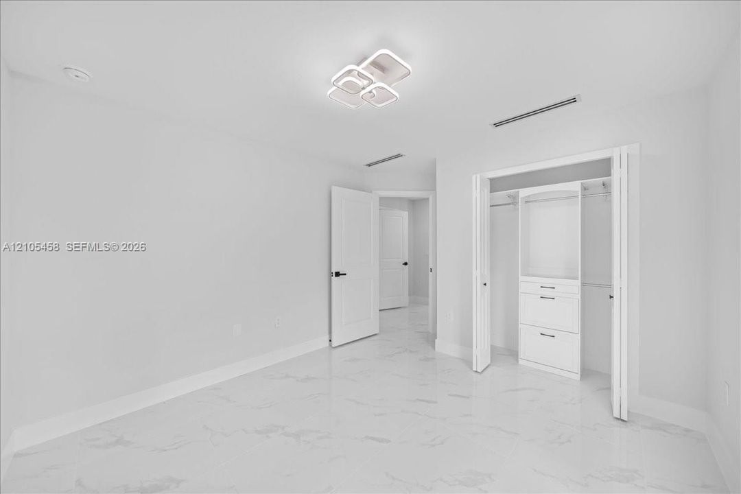 White tile flooring, contemporary ceiling light fixture, white interior doors, built-in closet organization system, recessed lighting