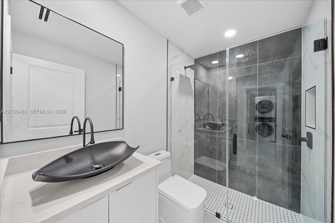 Modern bathroom featuring a glass-enclosed shower, vessel sink with matte black fixtures, white vanity cabinetry, and a light-toned countertop