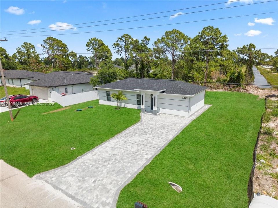 Modern exterior with light gray siding, dark roof, and a paver driveway