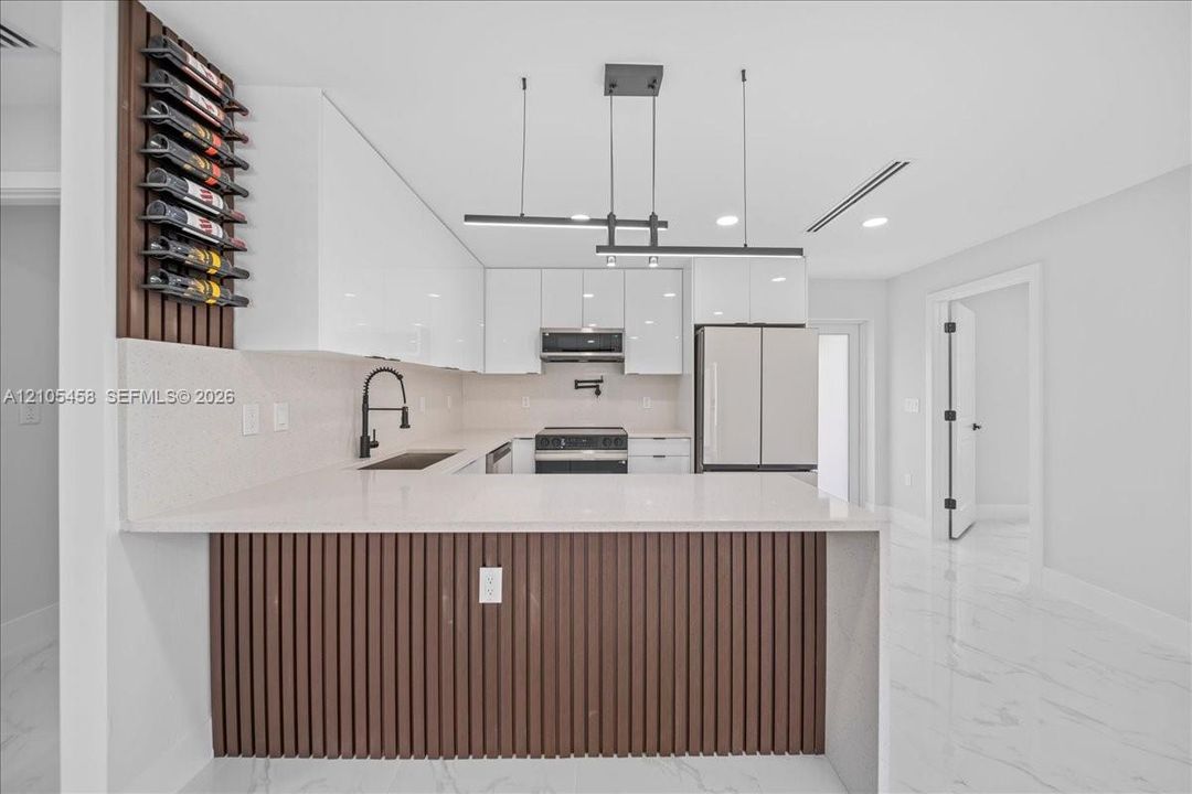 Modern kitchen featuring white cabinetry, light-colored countertops, stainless steel appliances, and wood-finish paneling on the kitchen island