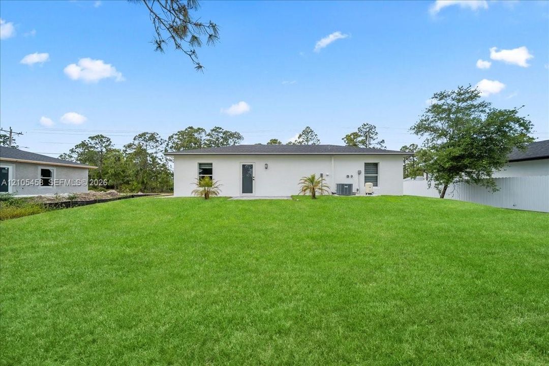 Expansive backyard featuring a manicured lawn, stucco exterior, and a privacy fence