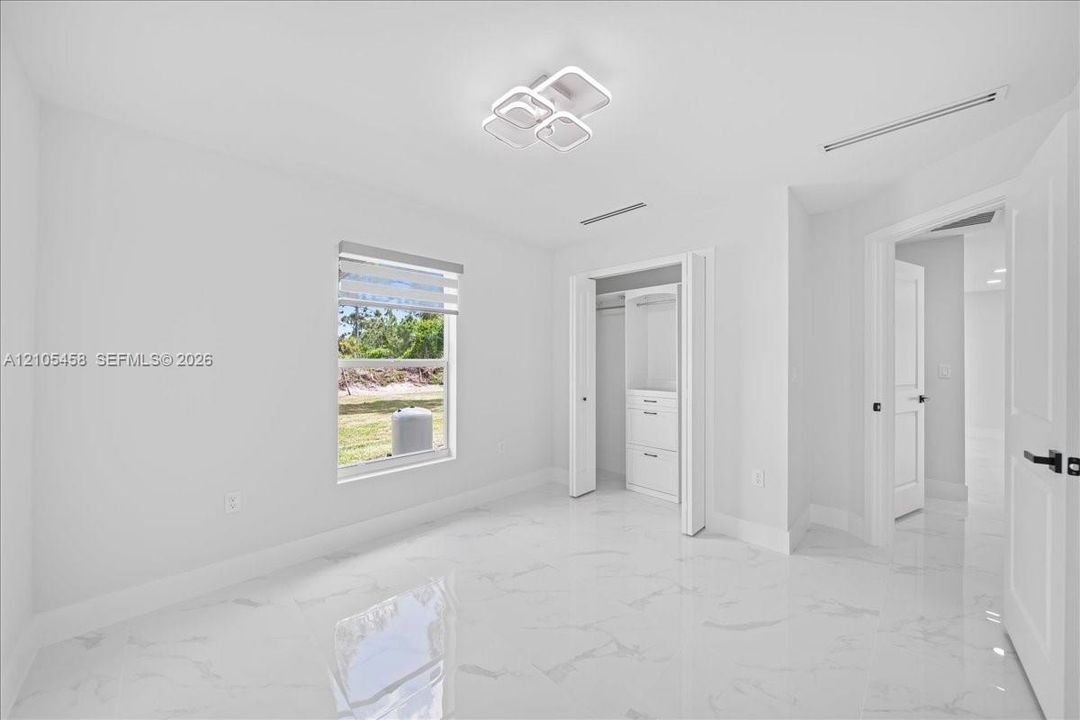 White tile flooring, modern ceiling light fixture, built-in closet storage, window with privacy blind, white panel doors