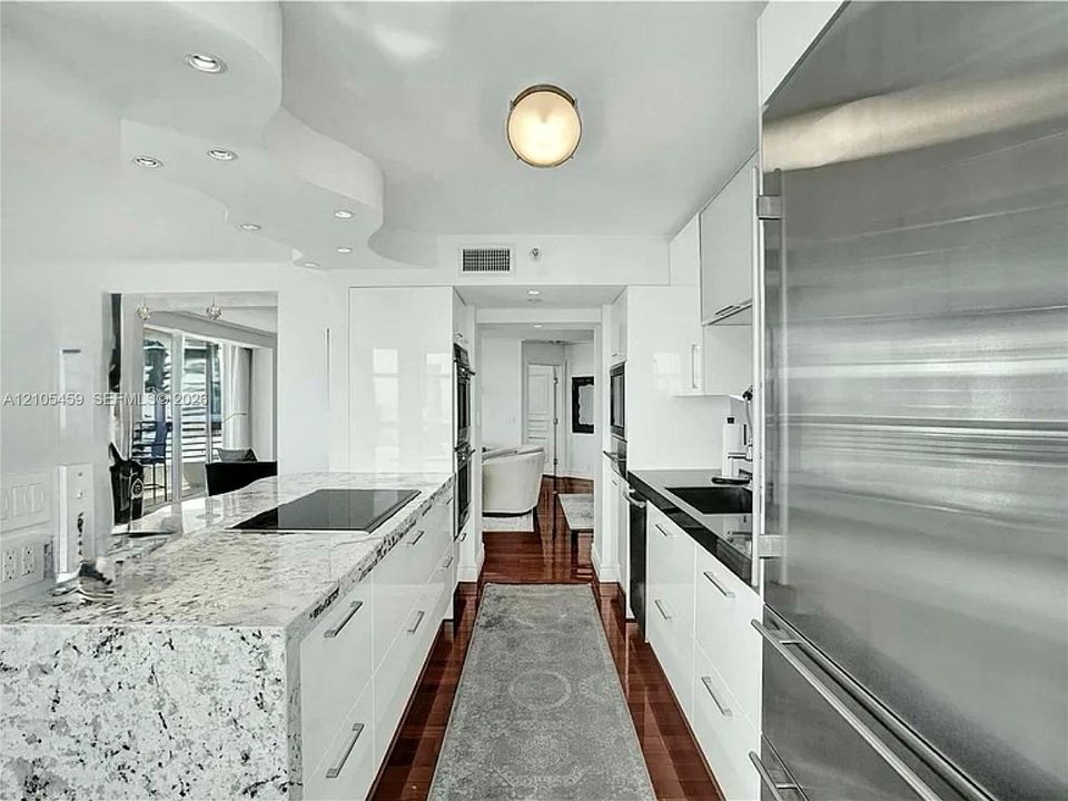 Modern kitchen featuring high-gloss white cabinetry, integrated stainless steel appliances, and wood-finish flooring