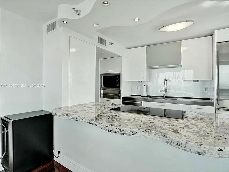 Kitchen featuring a curved stone countertop, built-in cooktop, white upper cabinetry, and a stainless steel oven