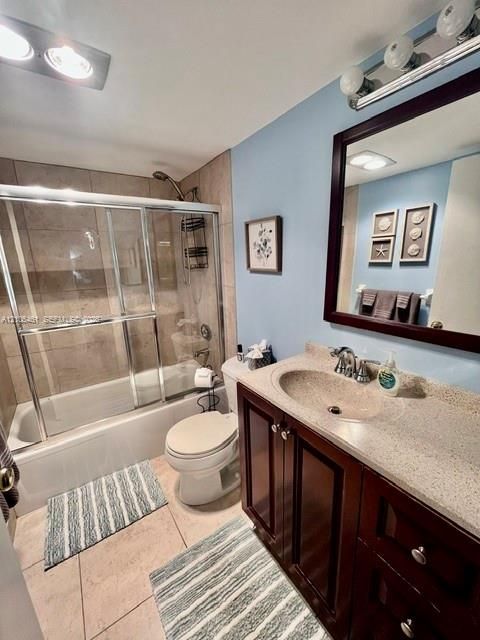 Tiled shower with sliding glass enclosure, integrated bathtub, stone-finish vanity countertop with built-in sink, dark wood-finish cabinetry, and tiled flooring