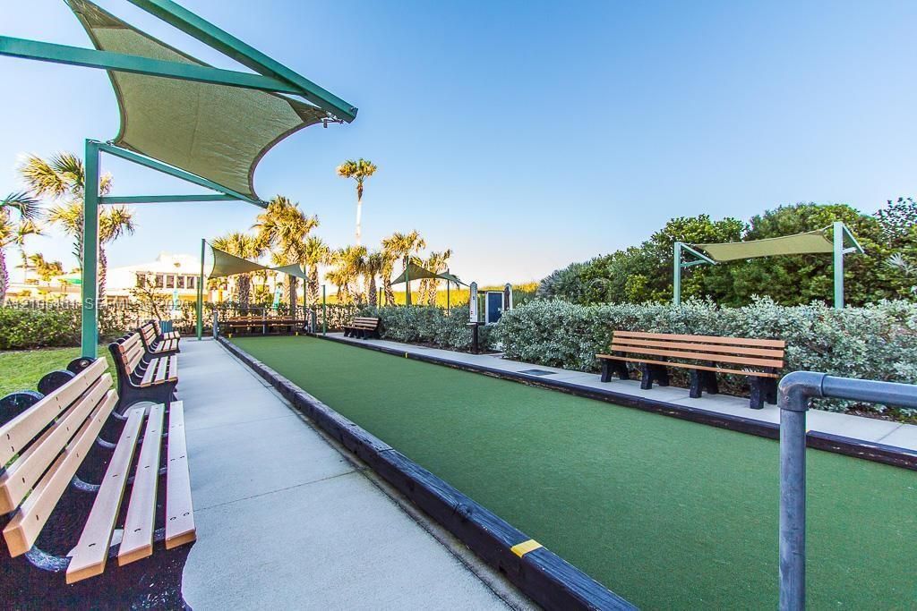 Bocce ball court featuring synthetic turf, reinforced timber borders, integrated shade structures, and wooden slat bench seating