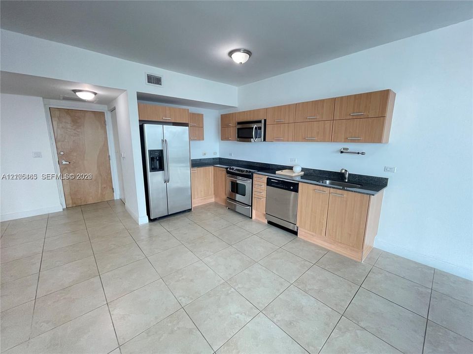 Kitchen featuring light wood-finish cabinetry, stainless steel appliances, dark countertops, and tile flooring