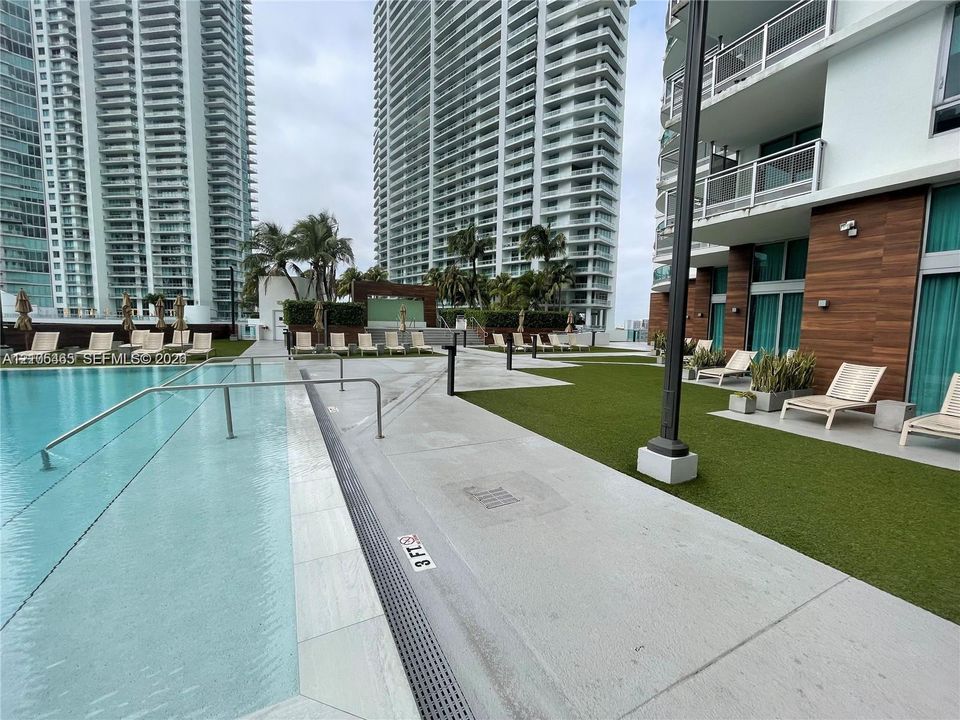 Swimming pool with a concrete surround, artificial turf accents, and a modern building exterior with wood-finish paneling