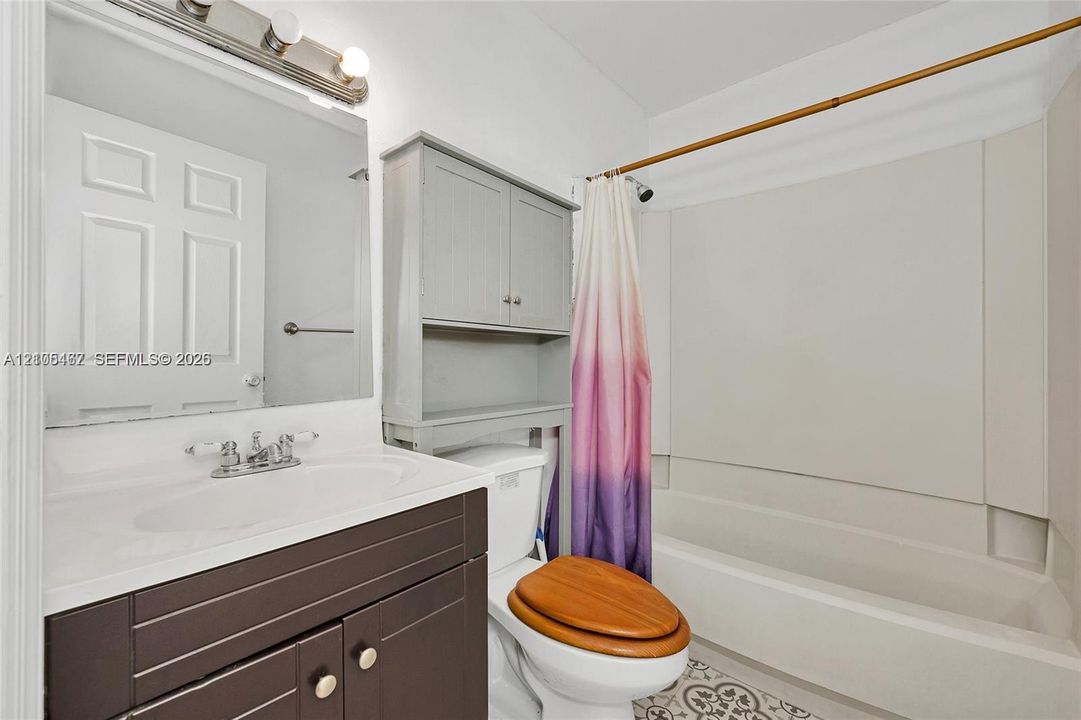 Bathroom featuring a vanity with integrated sink, over-the-toilet built-in cabinetry, wall-mounted mirror, three-light vanity fixture, and a tub-shower combination with surround