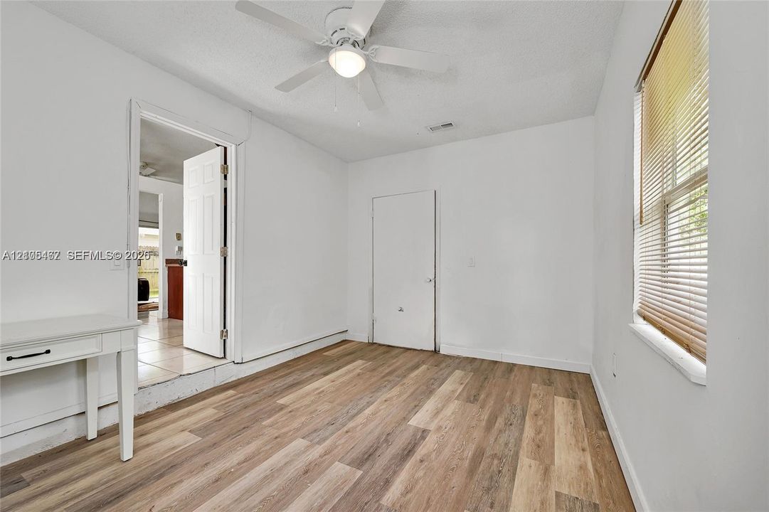 Room featuring wood-finish flooring, a white ceiling fan with integrated lighting, and a window with horizontal blinds