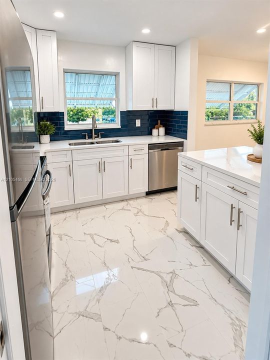 Kitchen featuring white shaker-style cabinetry, a white countertop, a blue subway tile backsplash, stainless steel appliances, and large-format porcelain tile flooring