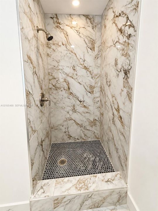 Walk-in shower featuring large format wall tiles with prominent veining, a mosaic tile shower pan, and a recessed ceiling light