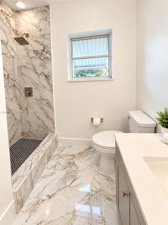 Walk-in shower with large-format marbled tile, recessed lighting, and a black mosaic tile shower floor