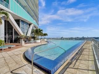 Infinity-edge pool with blue mosaic tile, surrounding paved decking, and integrated handrails