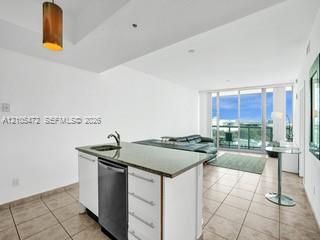 Kitchen island with an undermount sink and integrated dishwasher, tile flooring, and floor-to-ceiling sliding glass doors
