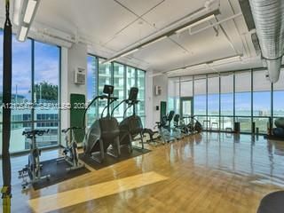Expansive room with wood-finish flooring, floor-to-ceiling windows, roller shades, exposed overhead ductwork, and track lighting