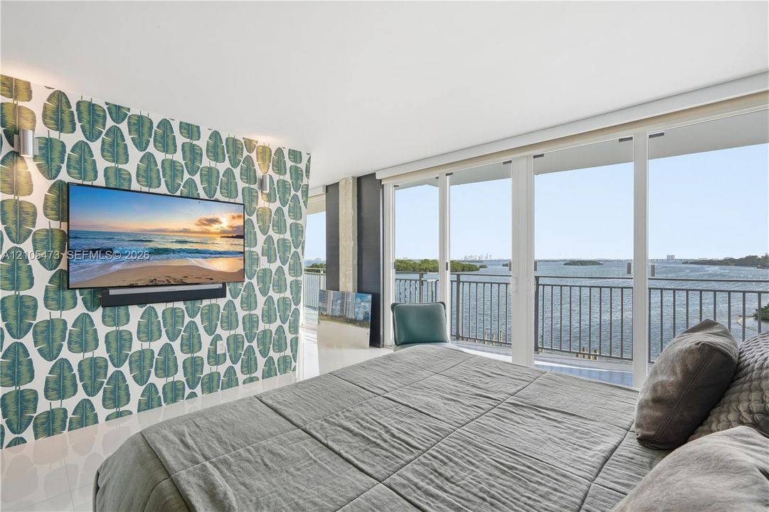 Floor-to-ceiling sliding glass doors, balcony with metal railing, water scenery, wall-mounted television, and decorative wall covering