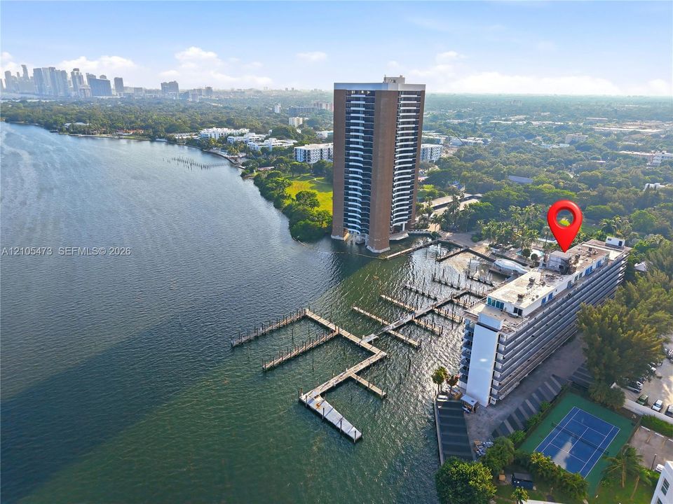 Waterfront property featuring extensive boat slips, a tennis court, and a high-rise building with multiple balconies