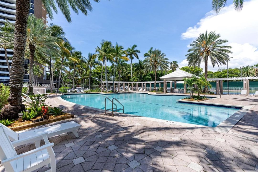 Swimming pool featuring a paved deck, built-in covered pavilion, pergola structures, and mature palm landscaping