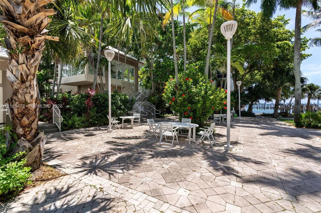 Extensive paved patio featuring geometric stone-paver hardscaping, mature palm trees, integrated post lighting, and direct access to coastal grounds