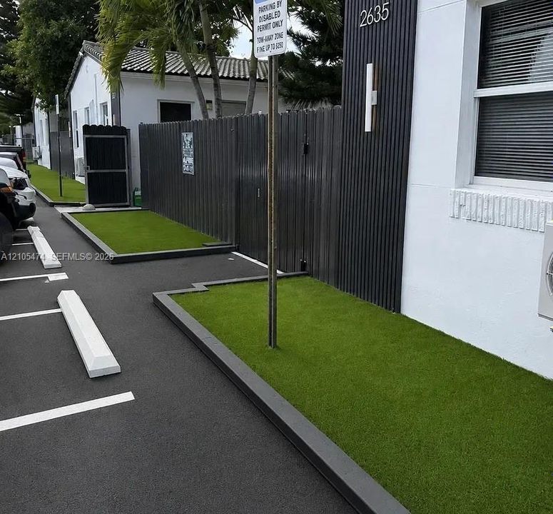 Off-street parking with painted spaces, artificial turf landscaping, dark fencing, and a building exterior with vertical paneling