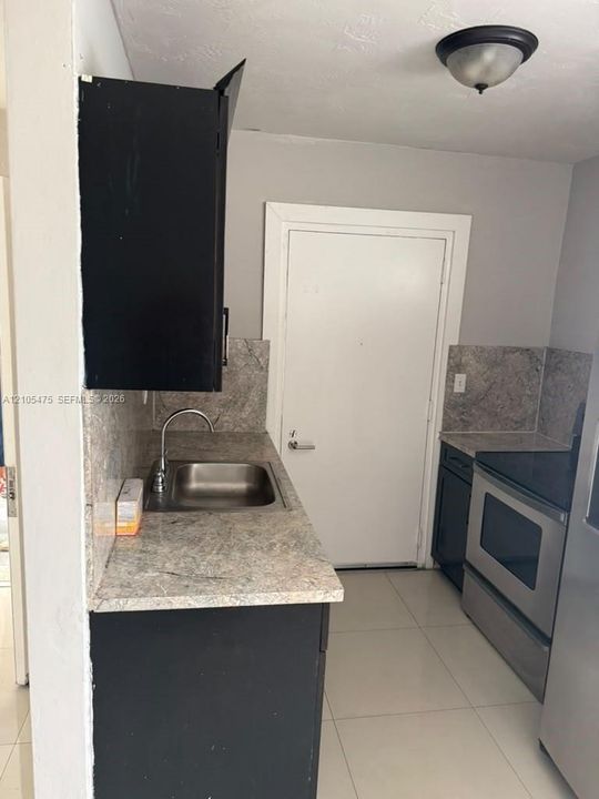 Kitchen area featuring dark-toned cabinetry, stone-patterned countertops, a stainless steel sink with a gooseneck faucet, tile flooring, and a stainless steel oven