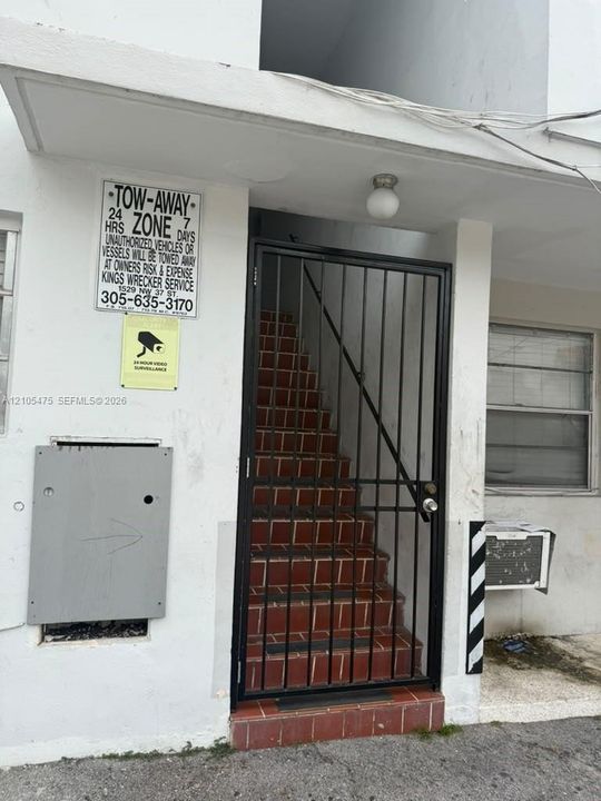Exterior entryway featuring a metal security gate, tile-surfaced stairs, and an overhead flush-mount light fixture