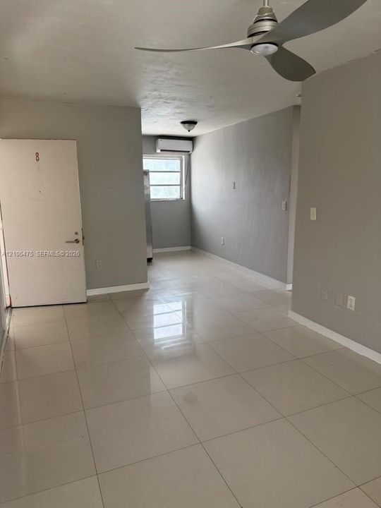 Large-format tile flooring, neutral wall tones, multi-blade ceiling fan, and wall-mounted ductless climate control unit