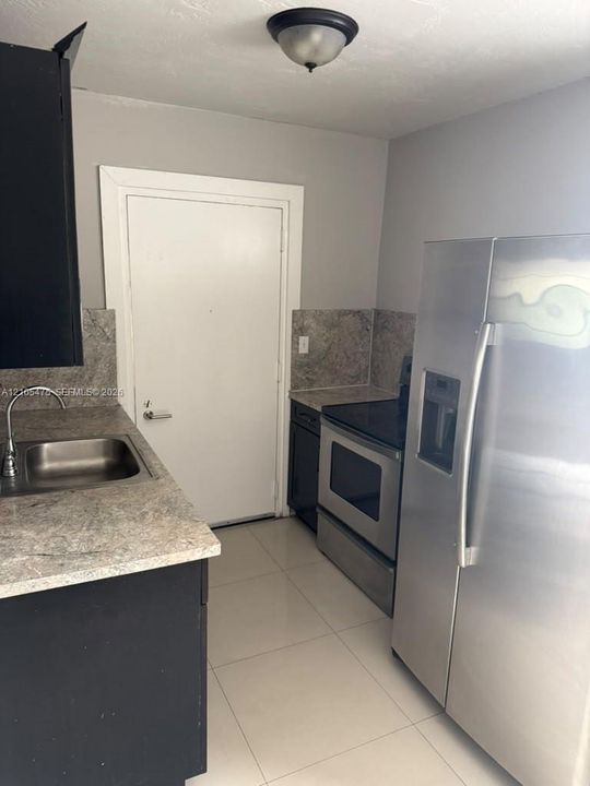 Kitchen featuring dark cabinetry, stone-surface countertops, tile flooring, and stainless steel appliances including a side-by-side refrigerator and smooth-top range