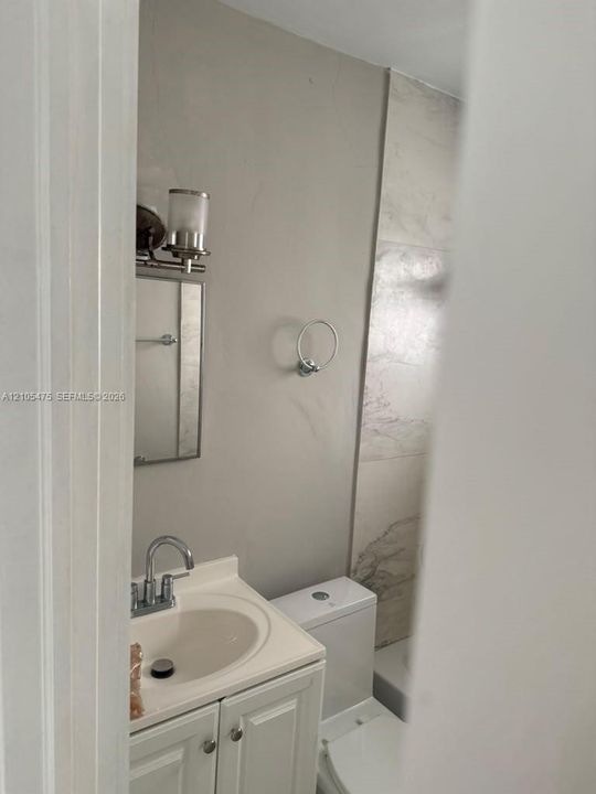 Bathroom featuring a vanity with an integrated basin, polished chrome faucet, wall-mounted lighting fixture, and large-format tile surround