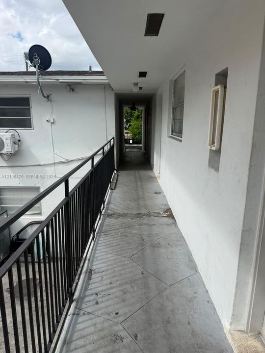 Exterior walkway featuring a concrete floor, black metal railing, and recessed ceiling lighting