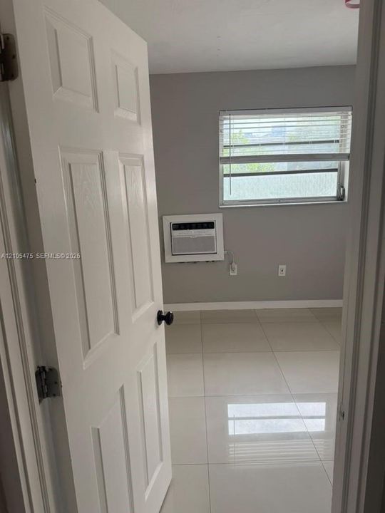 Room featuring large-format ceramic tile flooring, neutral wall paint, and a window fitted with horizontal blinds, complemented by a built-in wall-mounted air conditioning unit and a six-panel door