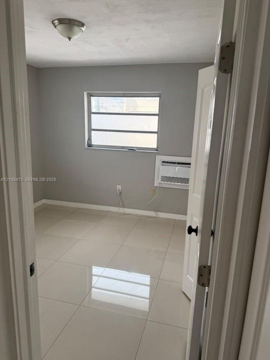 Room interior featuring neutral wall paint, polished large-format tile flooring, a multi-pane horizontal window, and a built-in window-mounted air conditioning unit