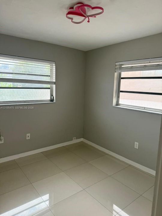 Neutral-toned interior featuring large-format ceramic tile flooring, two louvered windows, and a decorative flush-mount ceiling fixture