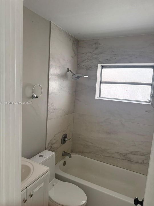 Bathroom featuring floor-to-ceiling neutral patterned tile surround, white tub, integrated vanity with an inset basin, and chrome fixtures