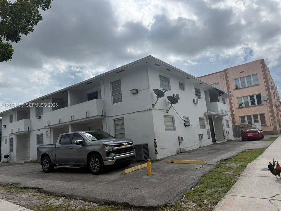 Multi-story residential building exterior featuring a white stucco facade, flat roofline, and dedicated paved surface parking