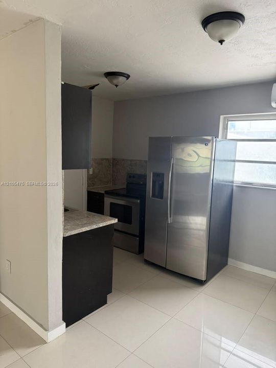 Kitchen featuring dark cabinetry, stone-finish countertops, stainless steel appliances, and large-format tile flooring