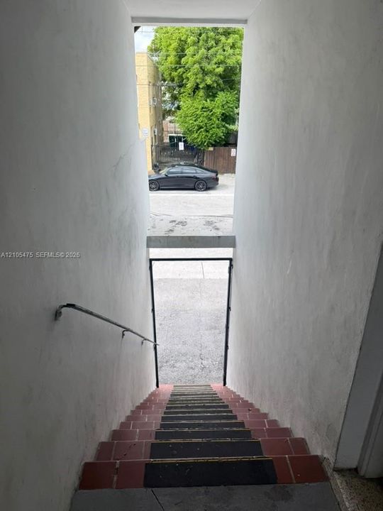 Exterior stairwell featuring red tile steps with non-slip treads and a wall-mounted metal handrail