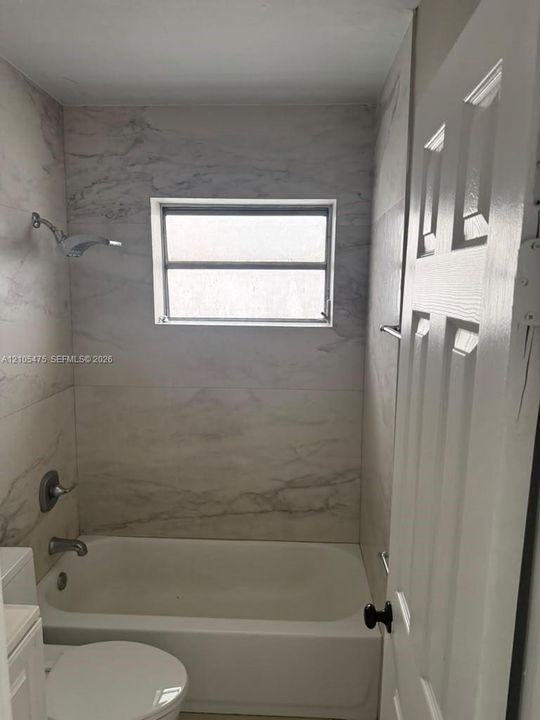 Bathtub surround featuring large-format veined tile, single-handle shower fixture, horizontal window, and six-panel interior door