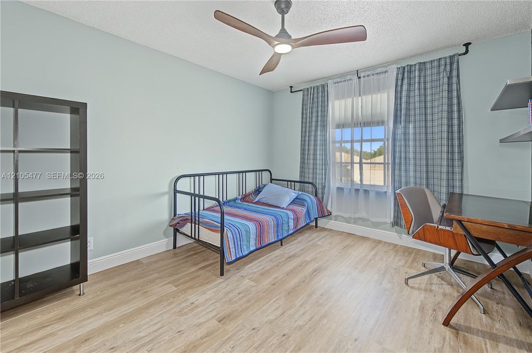 Light wood-finish flooring, built-in shelving, a ceiling fan with integrated lighting, and a window with natural light