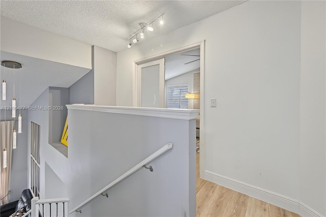 Stairwell with wood-finish flooring, white baseboards, and a contemporary pendant light fixture