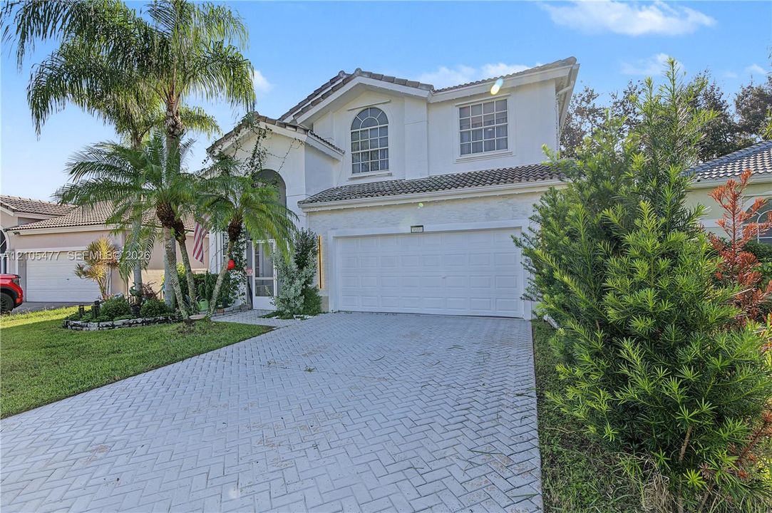 Two-story stucco exterior with a tiled roof, arched entry, and a paver driveway