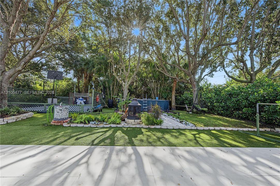 Expansive backyard featuring artificial turf, mature trees, a privacy fence, and defined landscaping beds